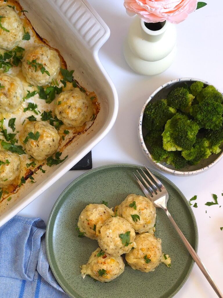a plate with baked chicken meatballs next to a bowl with steamed brocolli and a white ceramic baking dish