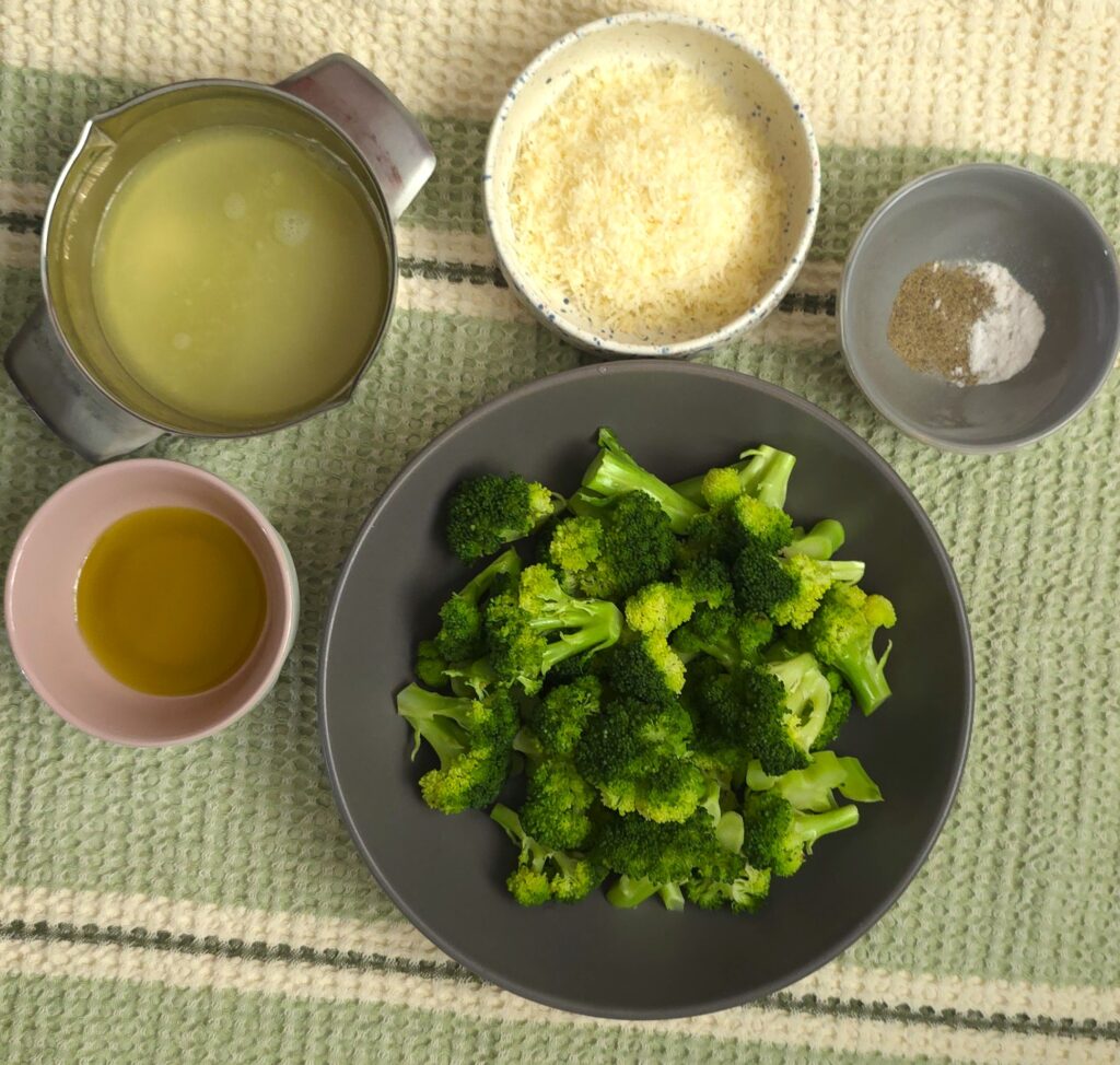 steamed broccoli with lemon and parmesan in a grey bowl next to fresh squeezed lemon juice, freshly grated parmesan, olive oil, salt and black pepper in bowls