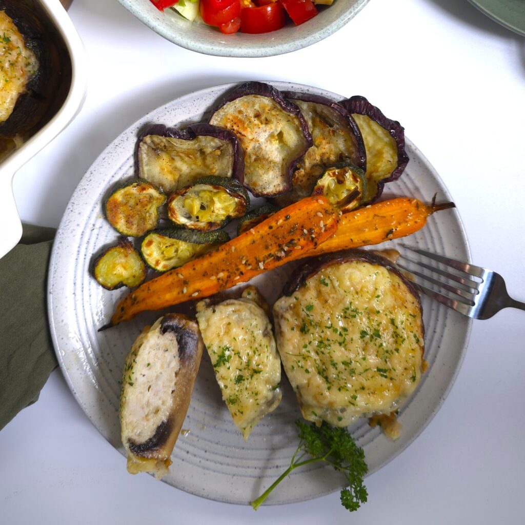 Baked portobello mushrooms stuffed with juicy chicken mince and topped with golden melted cheese, served hot with colourful roasted vegetables.