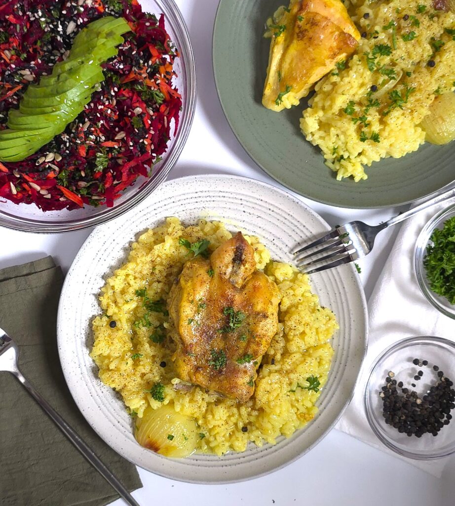 two plates with chicken with rice next to a bowl with a beetroot carrot avocado salad