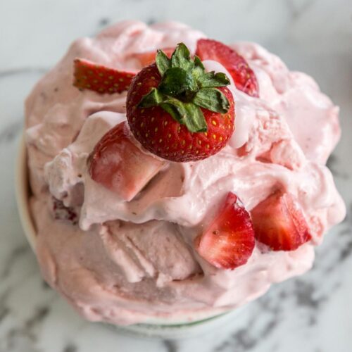 A bowl of homemade strawberry ice cream with fresh strawberries on a marble countertop.