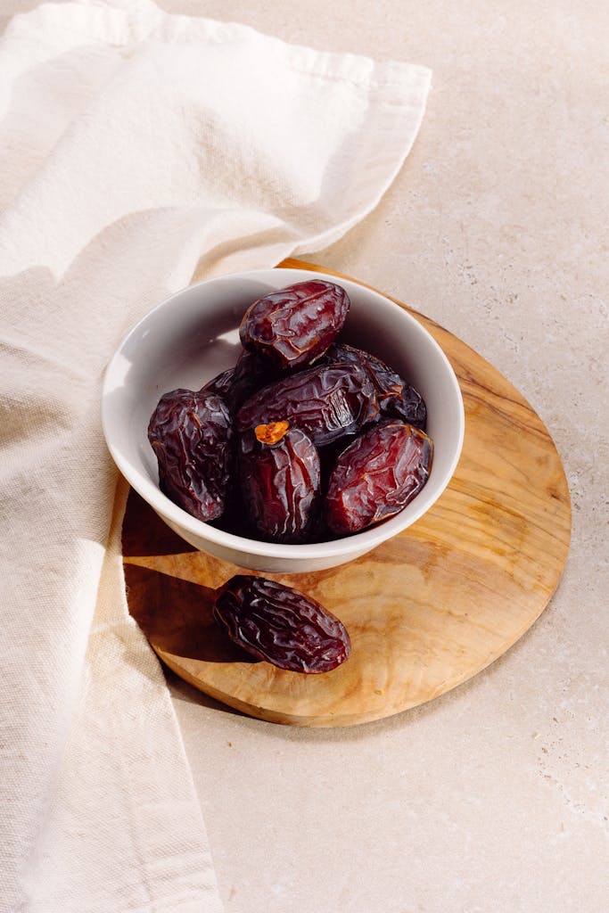 A minimalist still life of dates in a ceramic bowl on a wooden board.