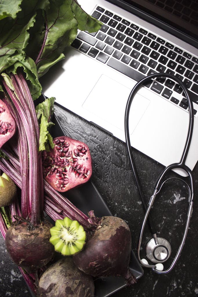 Flat lay of fresh vegetables, fruits, stethoscope, and a laptop promoting healthy lifestyle