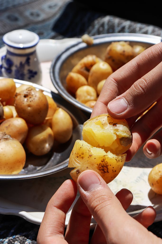 Hands peeling and handling boiled potatoes on a sunny day, showcasing fresh ingredients.