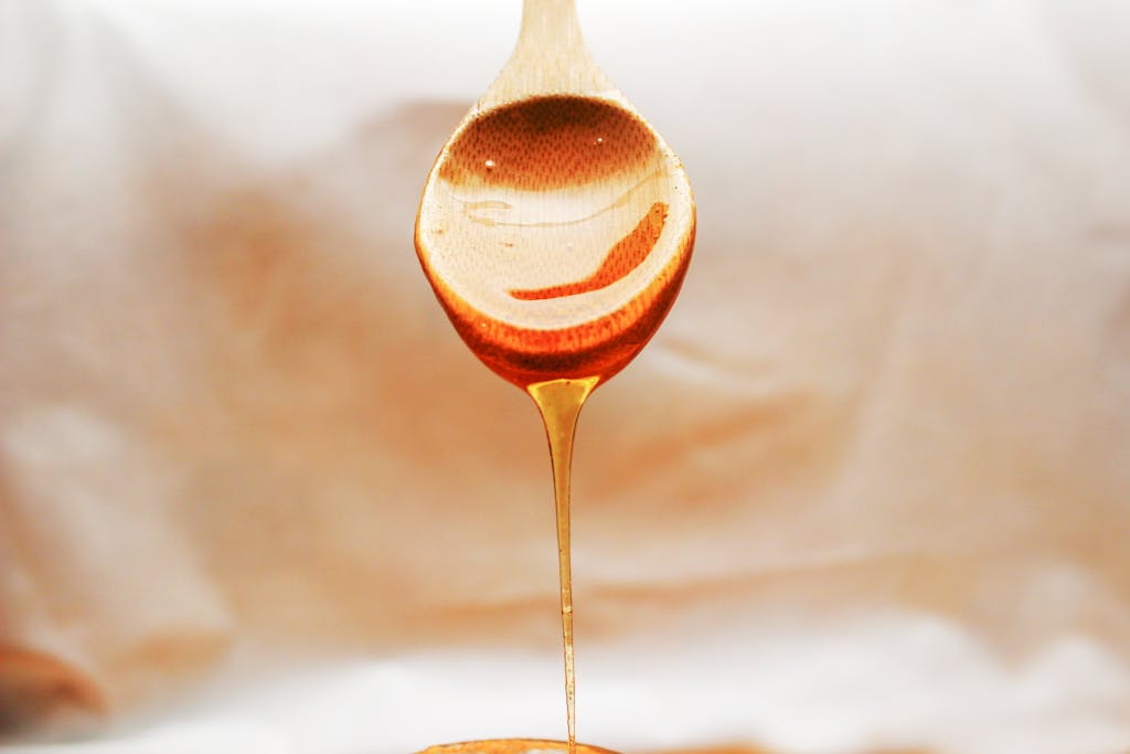 Honey drips from a wooden spoon in a warm and inviting still life setup.