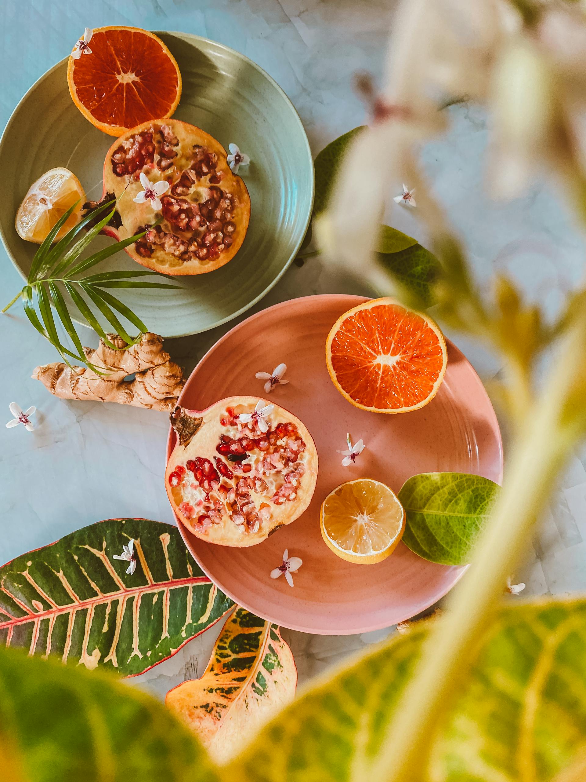 Overhead shot of sliced fruits and ginger on vibrant plates with leaves.