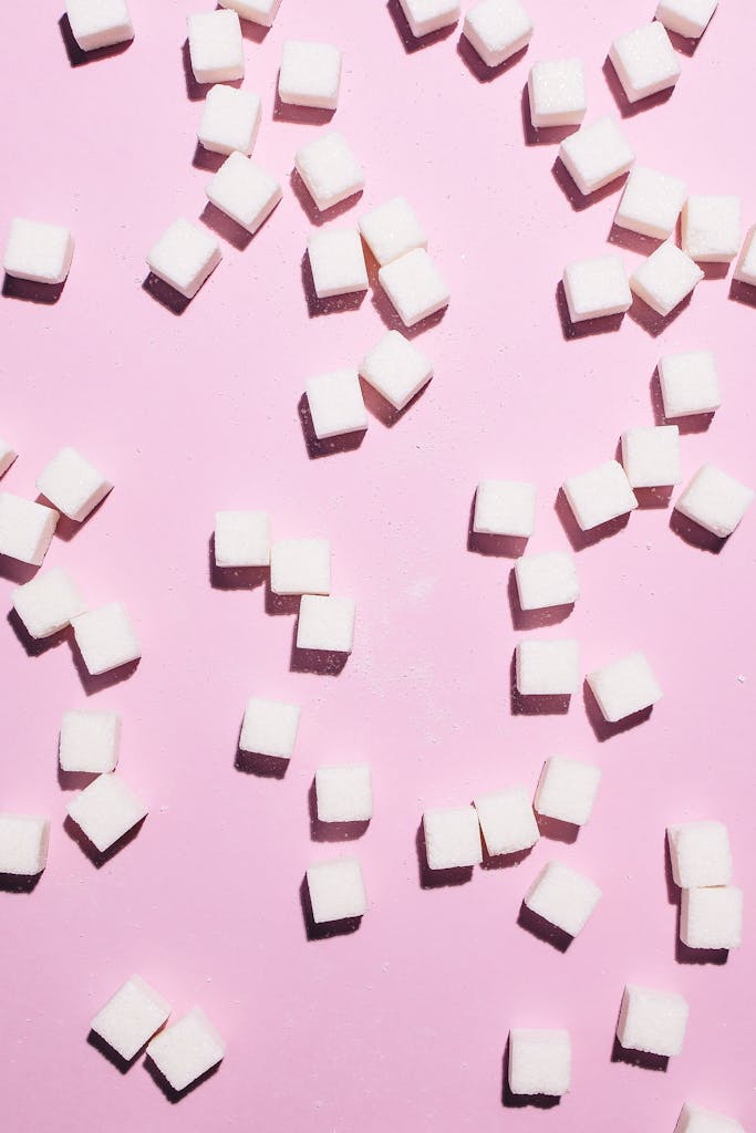 Scattered white sugar cubes on a pastel pink background perfect for food-related designs.