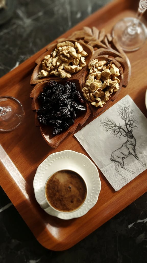 Top view of coffee, nuts, and prunes on a stylish wooden tray with an artistic napkin.
