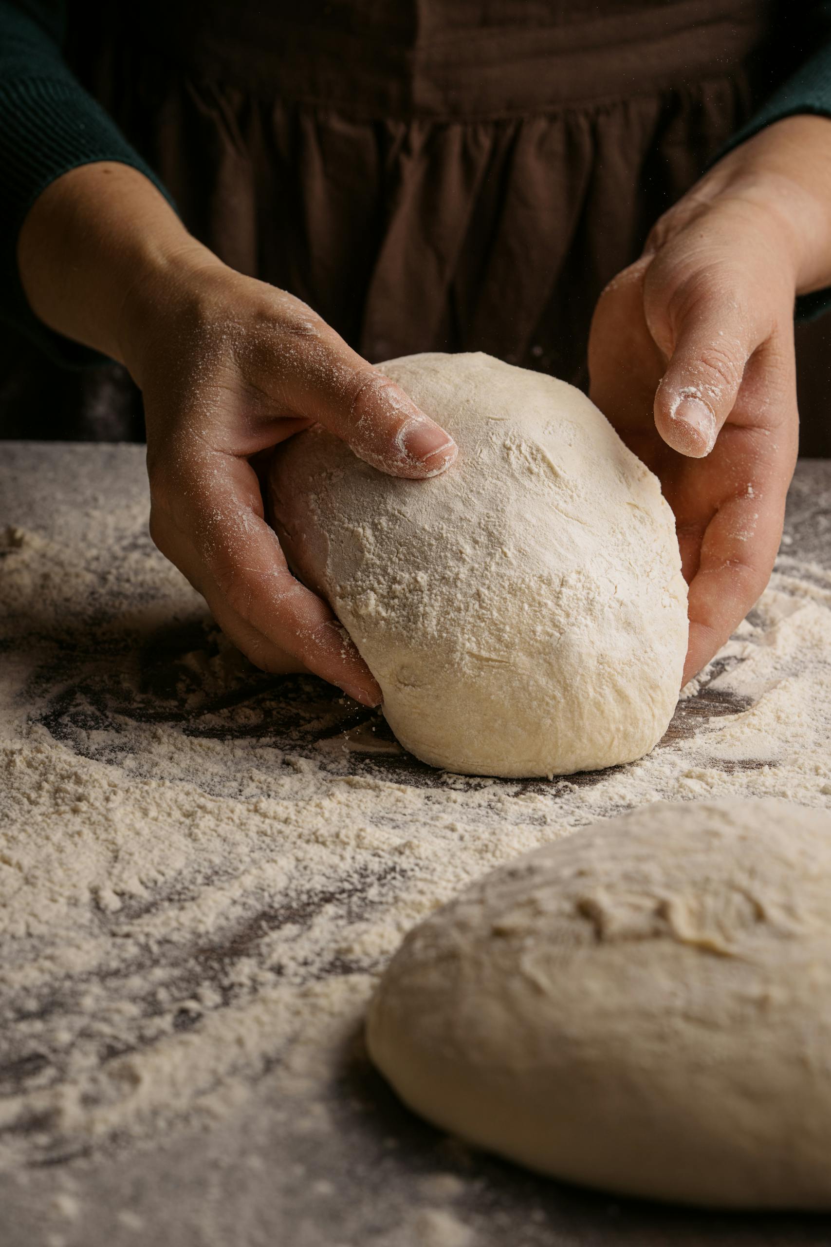 Gluten-free bake scene - a baker's hands kneading fresh dough on a floured surface for bread making.