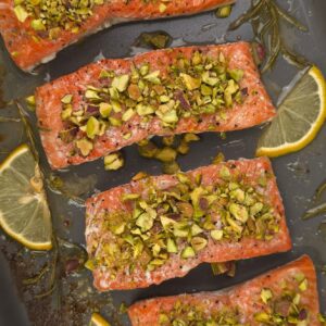 a close look of golden baked wild salmon fillets topped with crushed pistachio in a tray