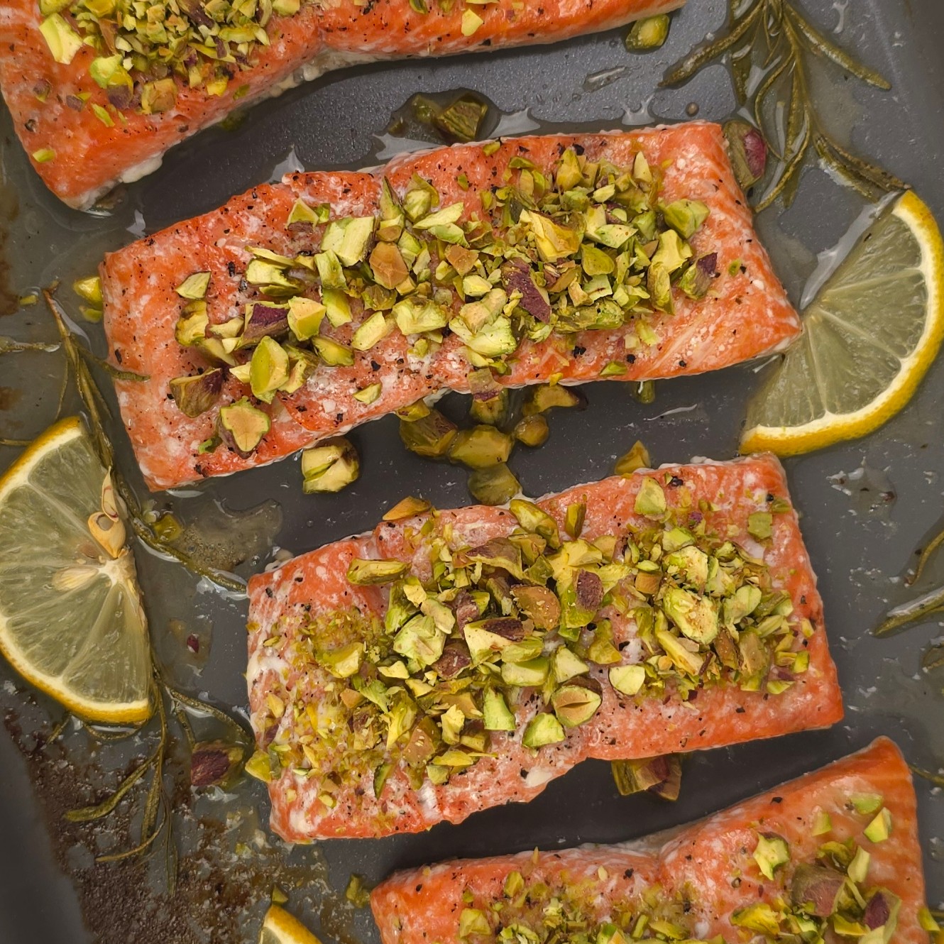 a close look of golden baked wild salmon fillets topped with crushed pistachio in a tray