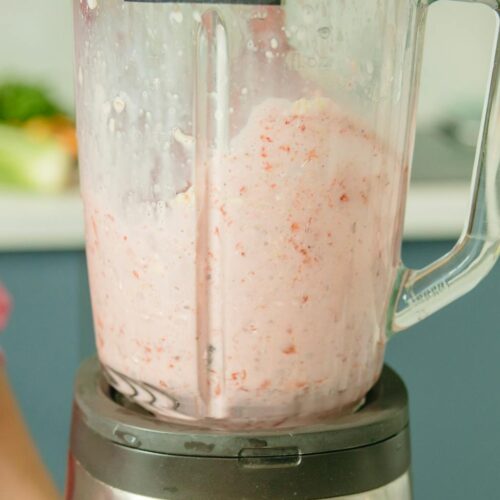 A person in pink attire using a blender to prepare a fresh fruit smoothie.
