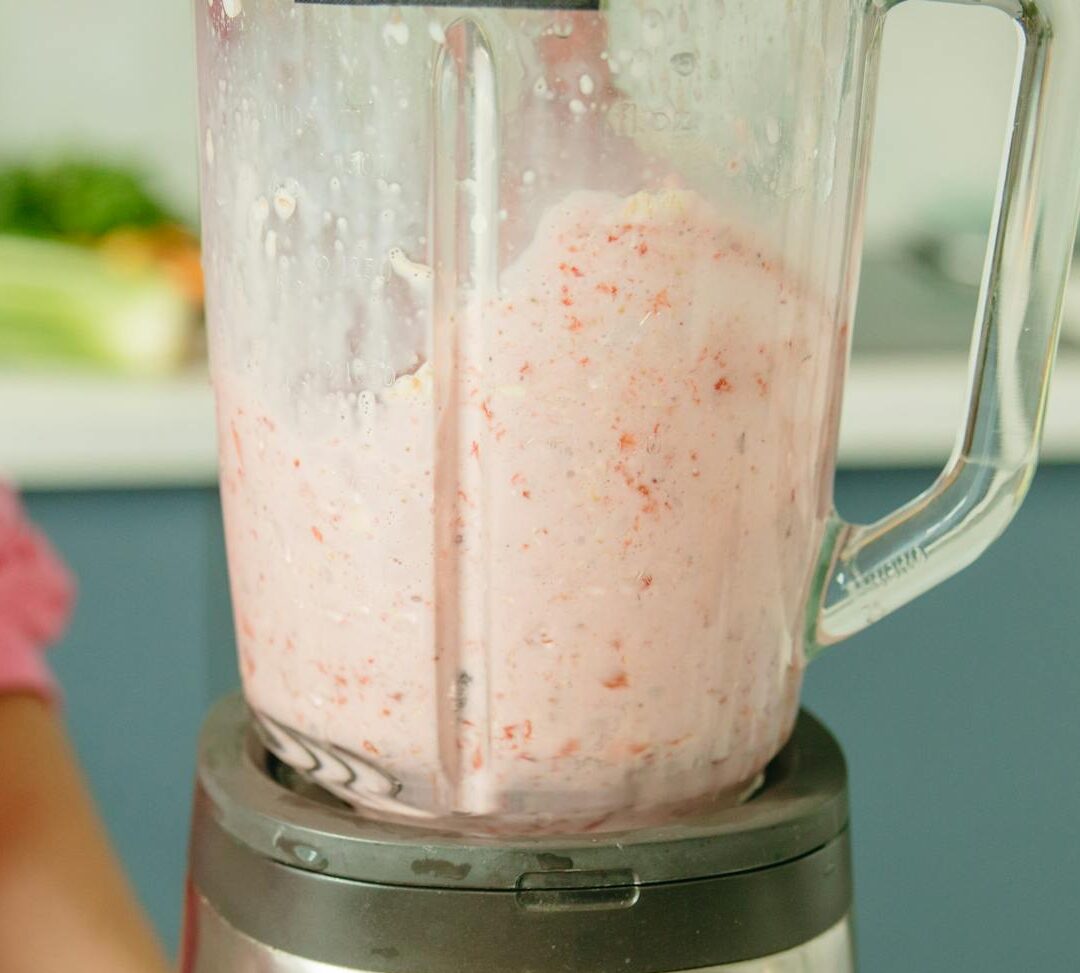 A person in pink attire using a blender to prepare a fresh fruit smoothie.