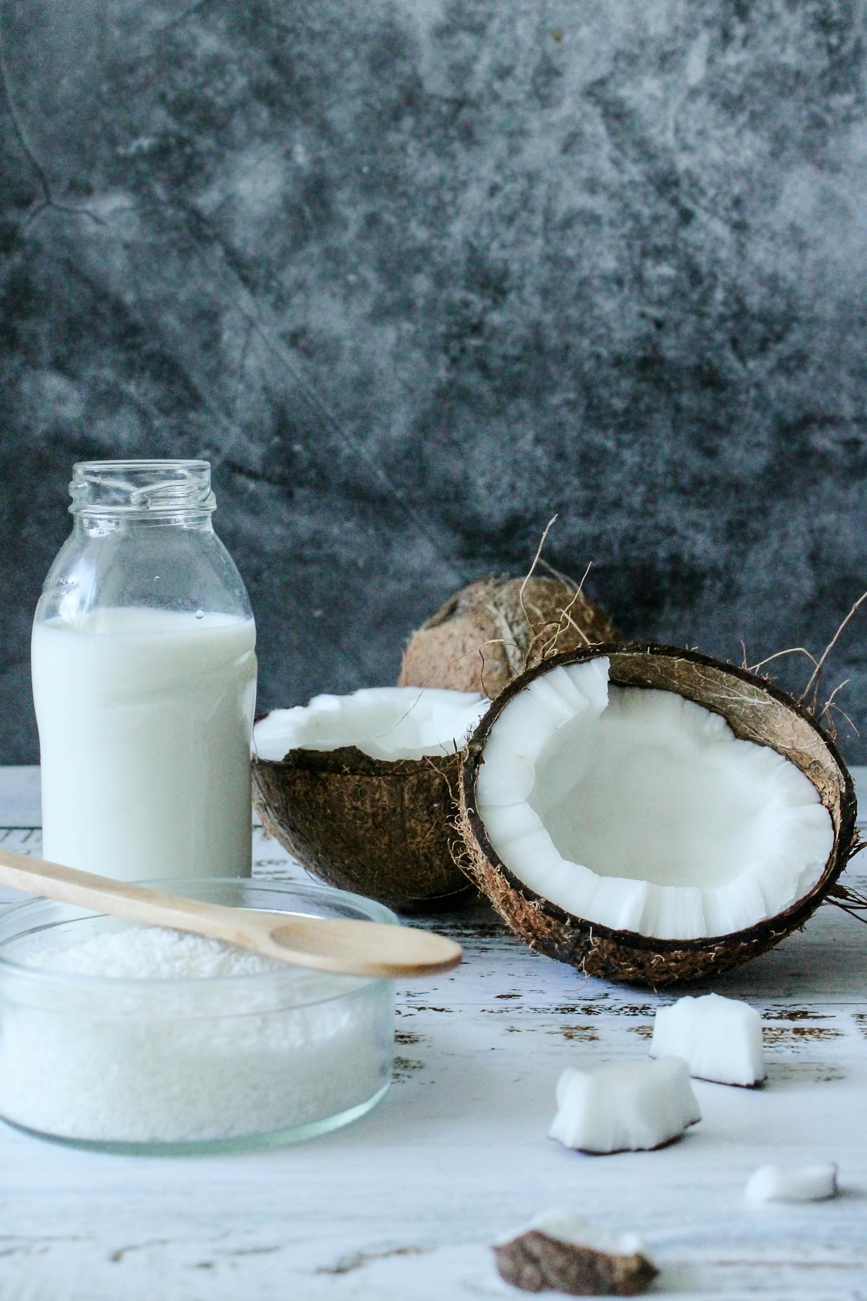 A rustic composition of fresh lactose-free coconut milk, shredded coconut, and coconut shells on a table.