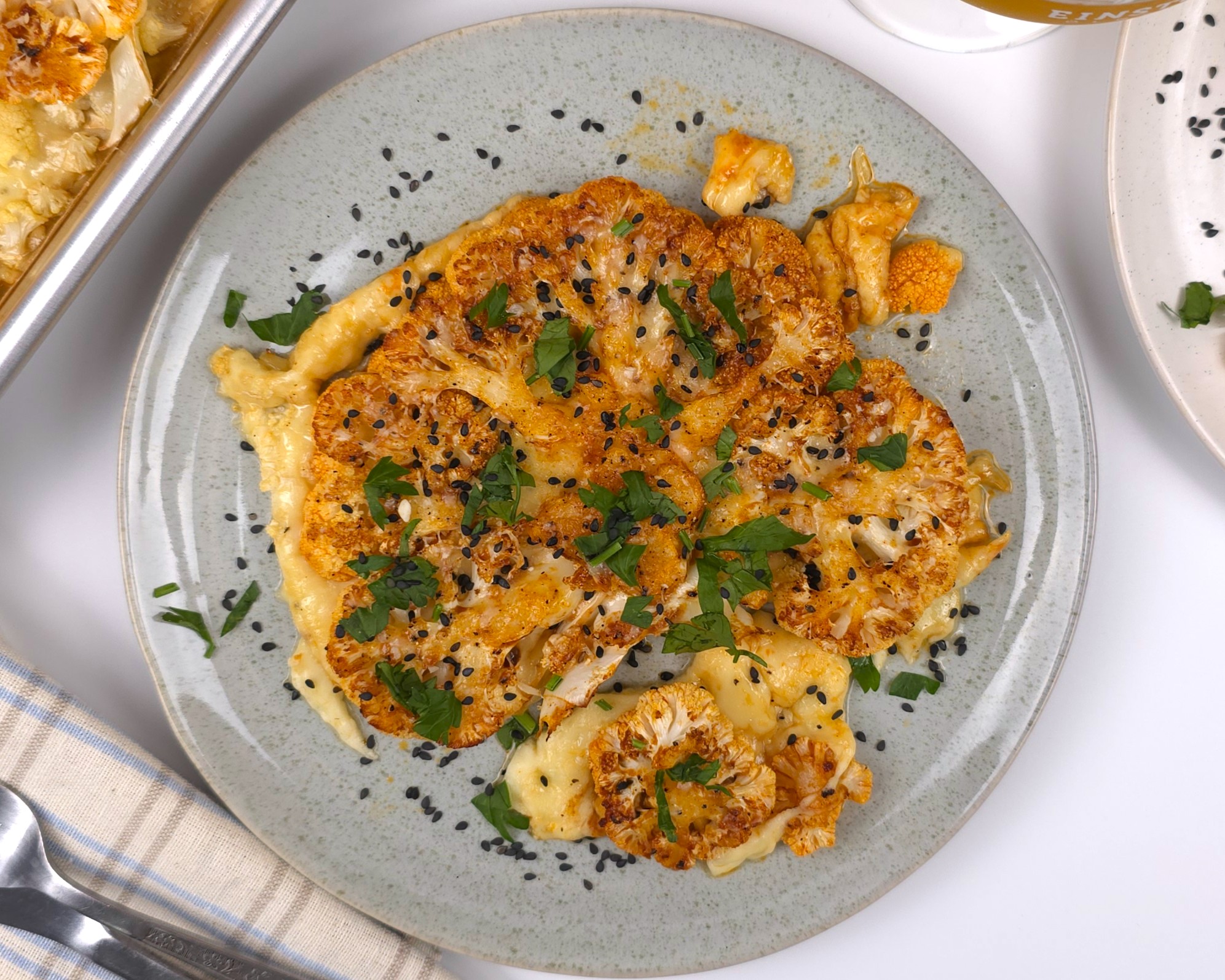 a golden baked cauliflower steak in a plate sprinkled with fresh parsley and black sesame