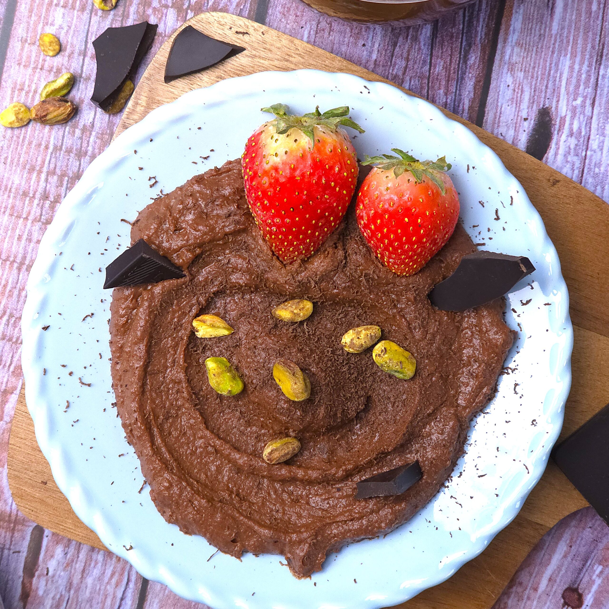 a blue ceramic plate with a homemade chocolate hummus, sprinkled with pistachios and strawberries