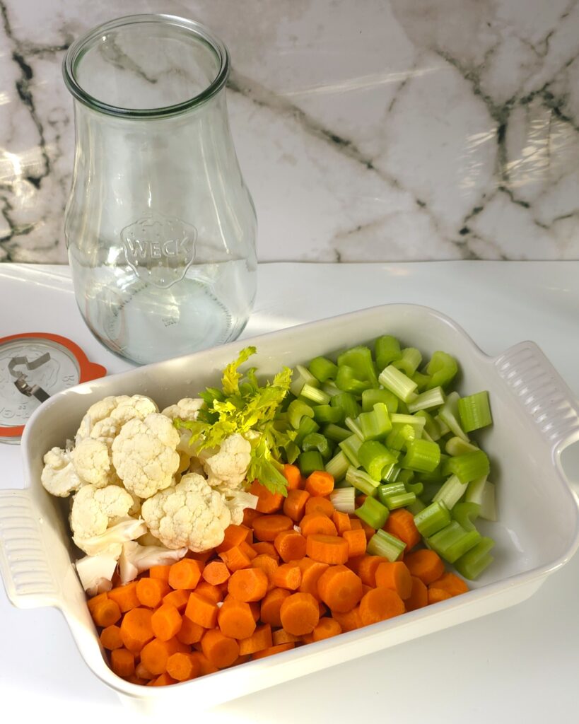 a tray with chopped carrots, cauliflower florets, celery sticks next to a preserving jar and a lid