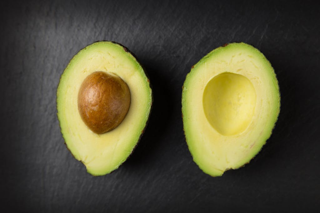 Close-up of fresh sliced avocado halves on a dark slate surface, showcasing healthy fats eating.