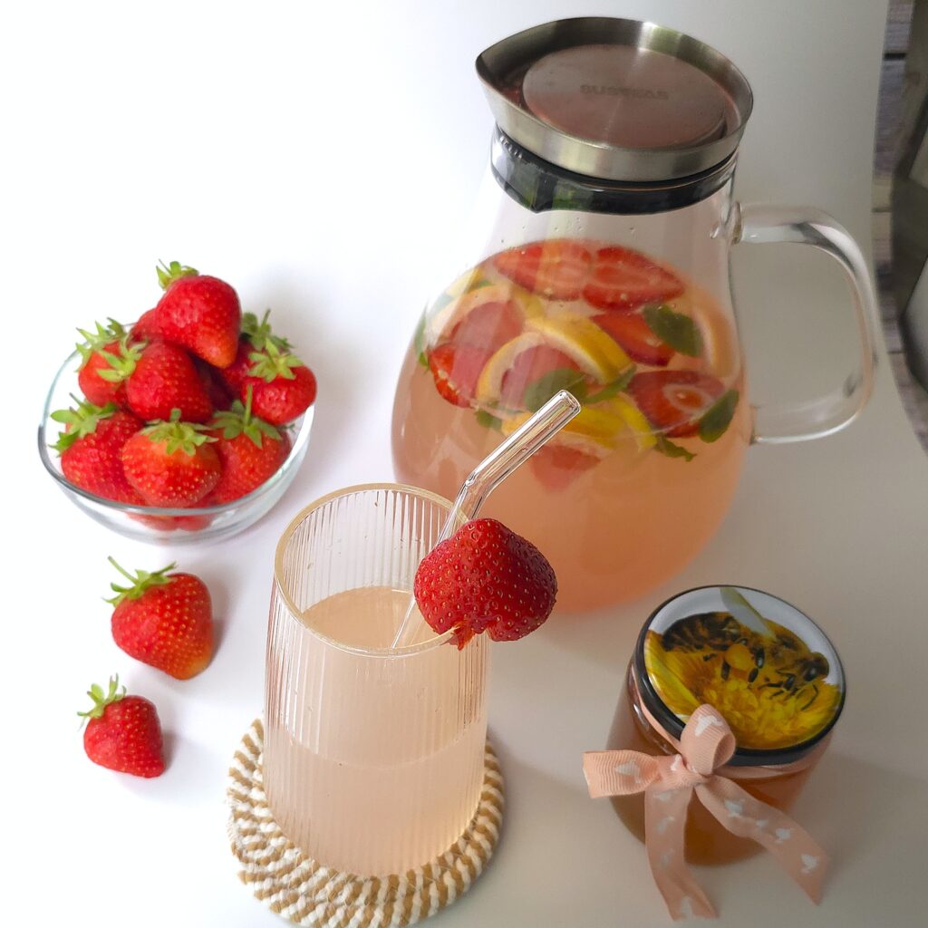 a glass of electrolyte drink next to a jug and bowl with strawberries