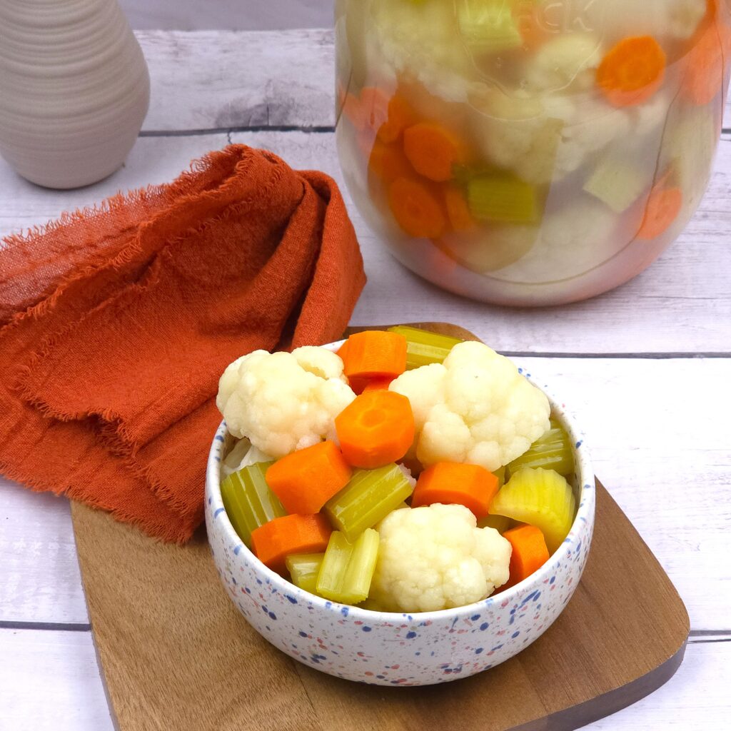 fermented cauliflower, carrots and celery sticks in a bowl next to a fermented jar