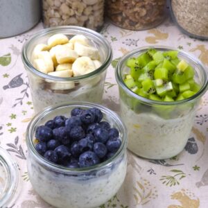 Gluten-free overnight oats layered with yoghurt, fruit, and nuts in glass jars, topped with blueberries, kiwi, and banana.