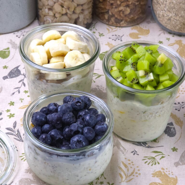 Gluten-free overnight oats layered with yoghurt, fruit, and nuts in glass jars, topped with blueberries, kiwi, and banana.