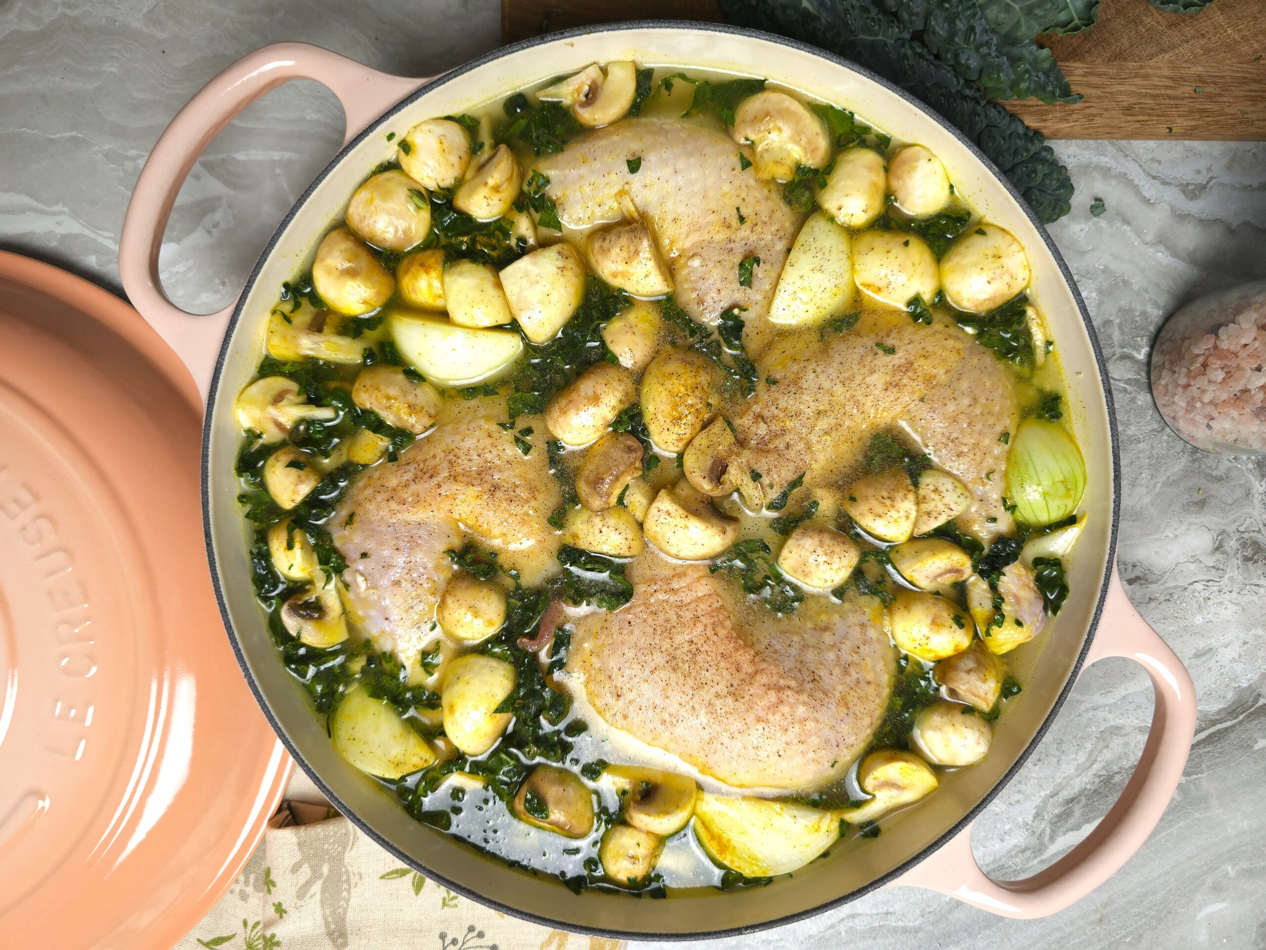a cast iron baking shallow dish with uncooked chicken legs with rice, kale, mushrooms and onion