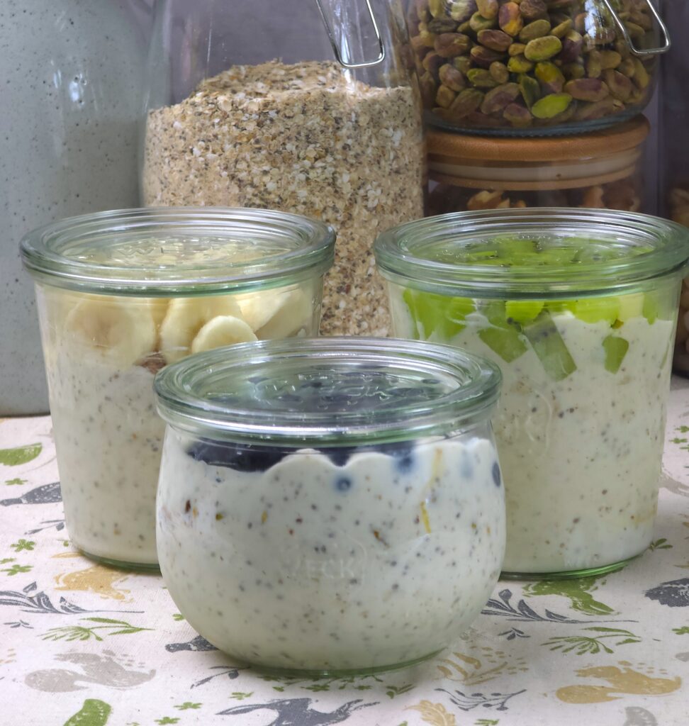 Gluten-free overnight oats layered with yoghurt, fruit, and nuts in glass jars with lids, topped with blueberries, kiwi, and banana.