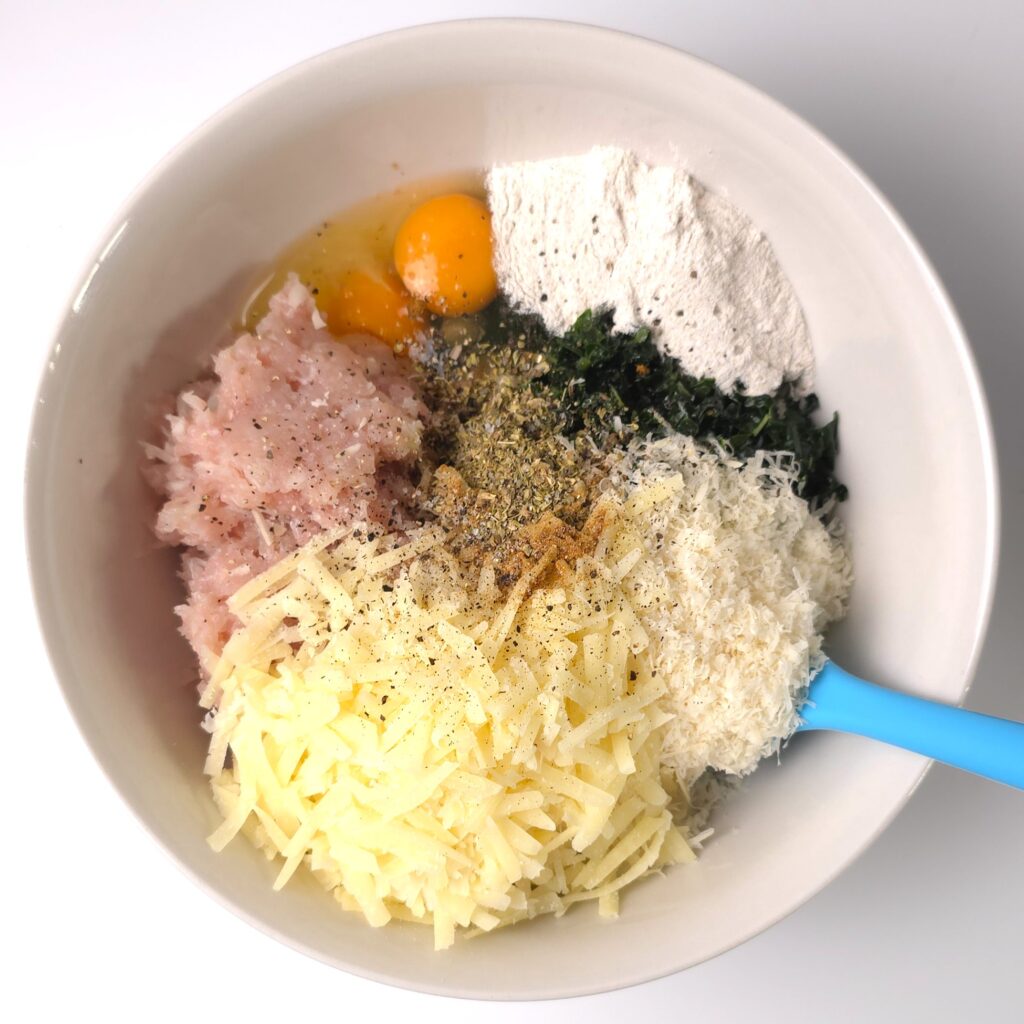 a mixing bowl with homemade turkey mince, grated lactose-free cheese, grated Parmigiano Reggiano, eggs, buckwheat flour, chopped kale and seasonings