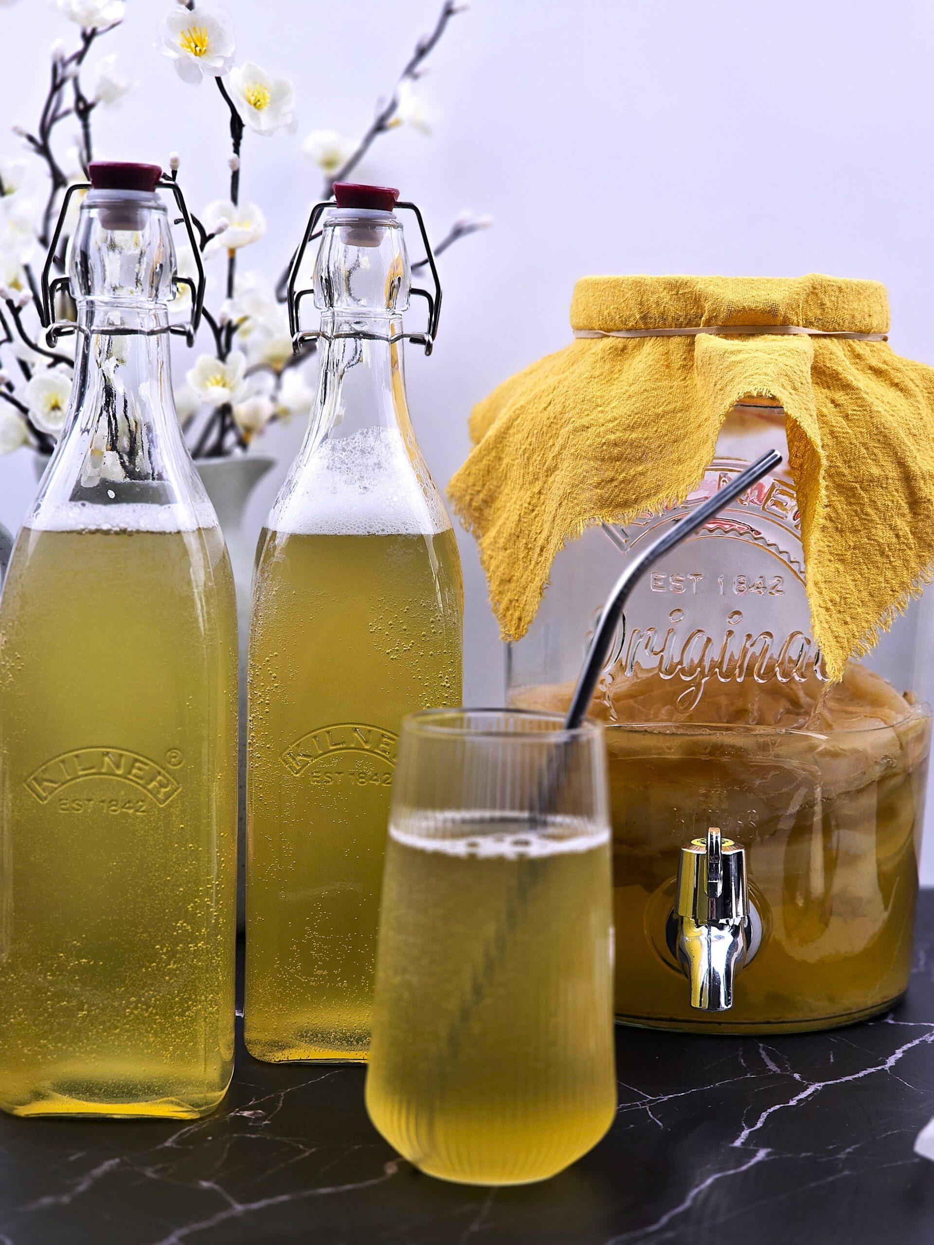 two bottles, a glass of kombucha next to 5L fermenting jar