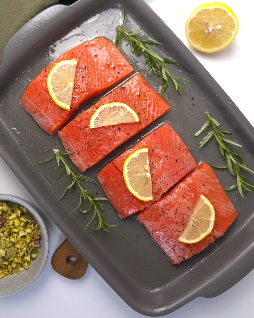 four wild salmon fillets in a baking tray, topped with lemon slices and rosemary wine sauce.