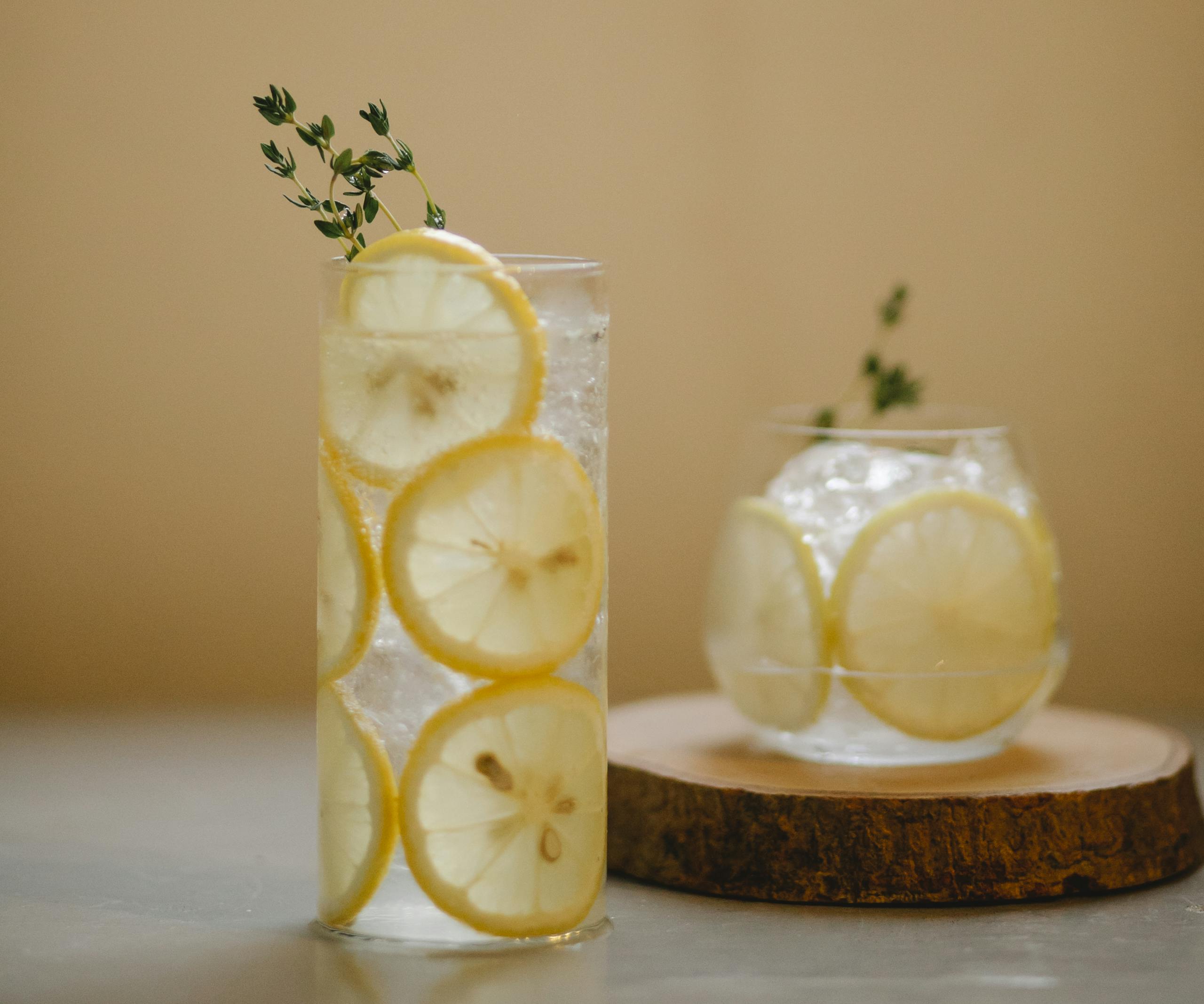A cool, refreshing detox myths and facts drink with lemon slices and thyme in clear glasses on a wooden coaster.