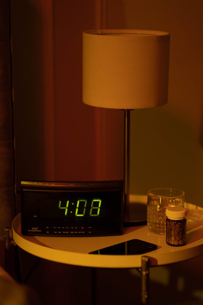 A warm and moody bedside table with a digital clock showing 4:08 in terms of midlife sleep problems and a lamp in dim lighting.