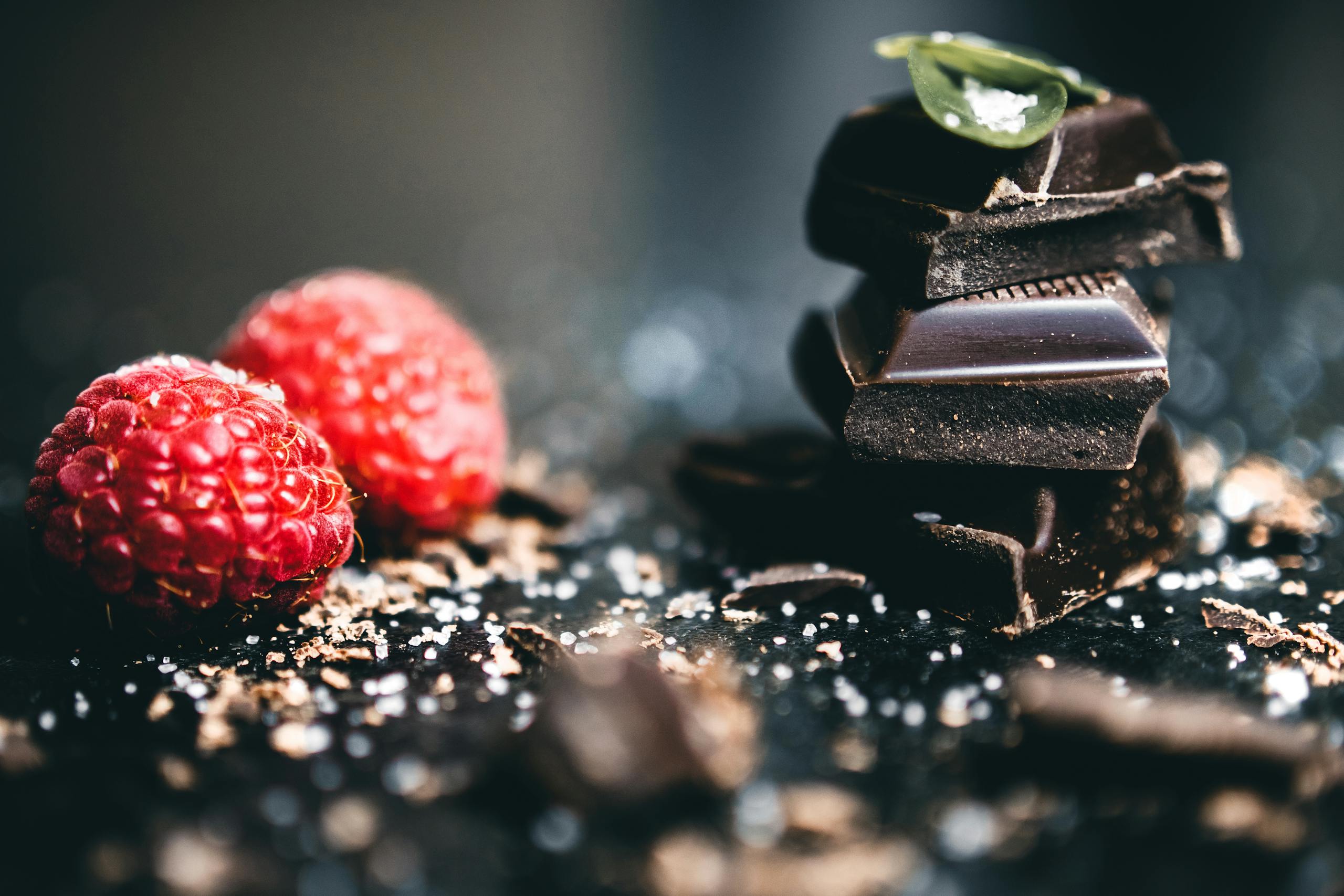 Artistic close-up of dark chocolate with a high cocoa health benefits, pieces with fresh raspberries, perfect for dessert visuals.