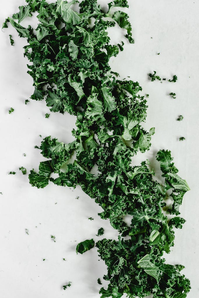 Close-up of fresh organic kale leaves scattered on a white surface, highlighting green textures.