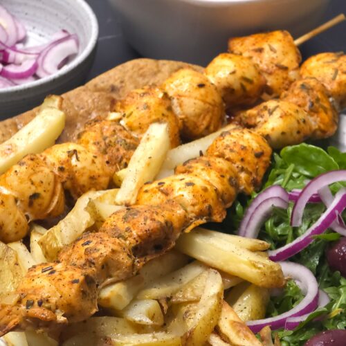 a closer look to greek chicken souvlaki in a plate along with sides