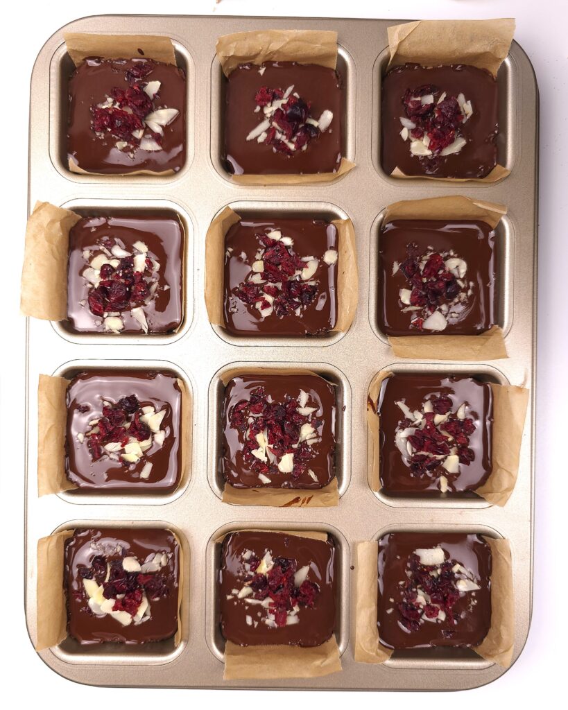 Almond cranberry bars in molds topped with melted dark chocolate and decorated with extra cranberries and shaved almonds
