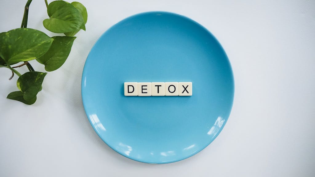 Minimalist concept of detox myths and facts with letter tiles on a turquoise plate and green leaves.