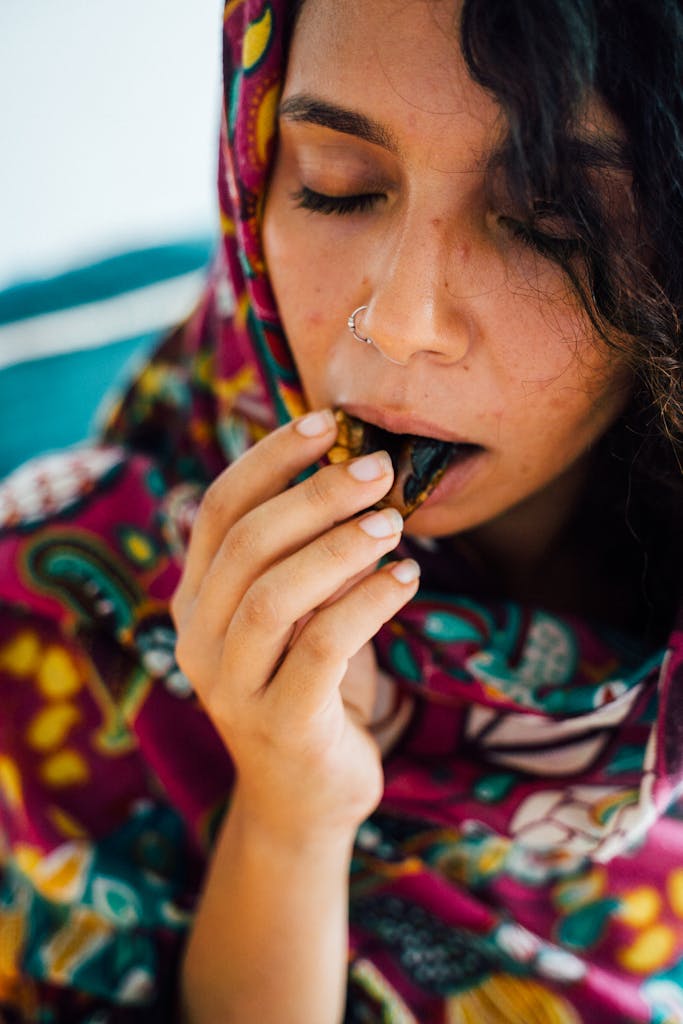 Portrait of a woman in colorful attire enjoying a piece of chocolate with eyes closed.