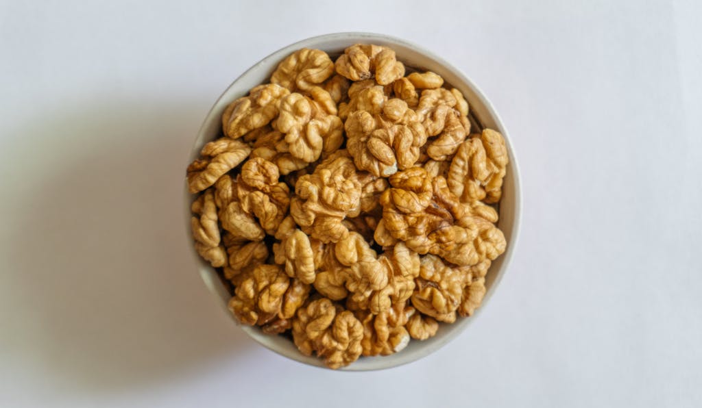 A bowl filled with fresh, shelled walnuts on a clean white background.