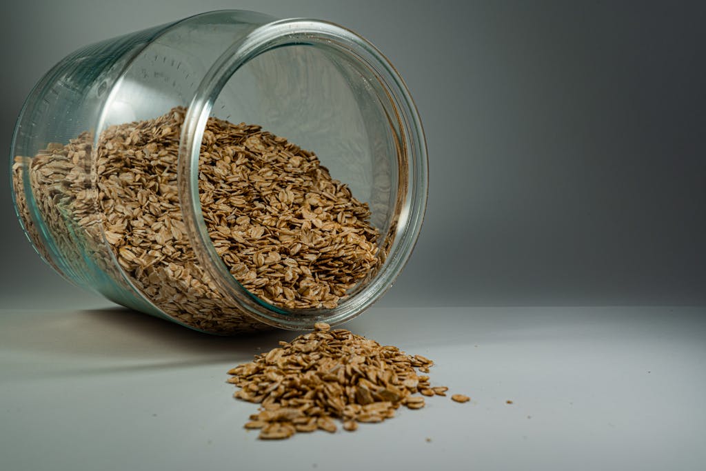 Are oats gluten-free - a glass jar spilling rolled gluten-free oats onto a plain surface, showcasing a rustic breakfast ingredient.