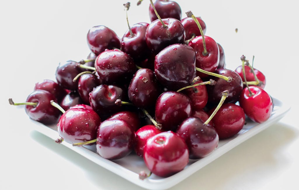 A pile of ripe, juicy red cherries on a white plate, showcasing their freshness.