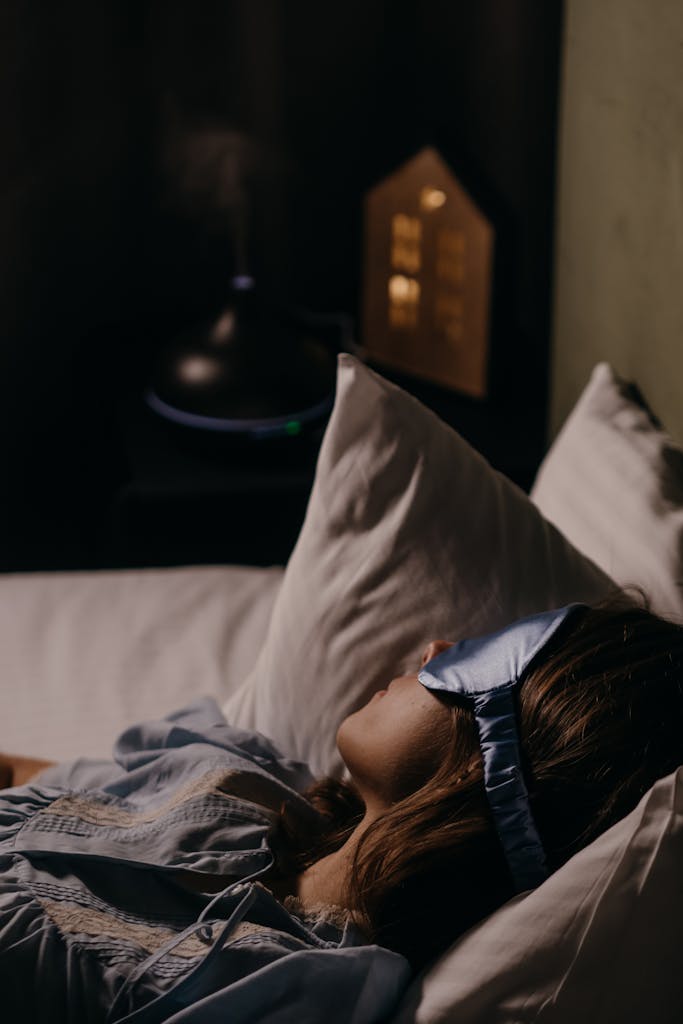 A woman wearing a blue eye mask sleeping comfortably in a cozy bedroom setting.