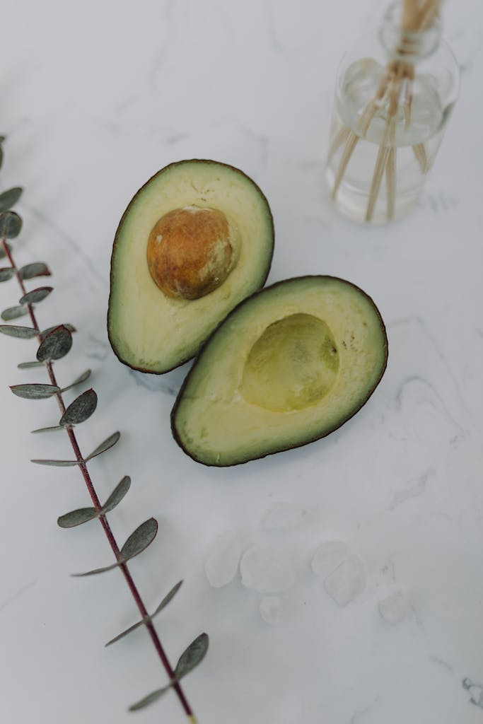 Close-up of a sliced avocado and eucalyptus leaves on a white surface.