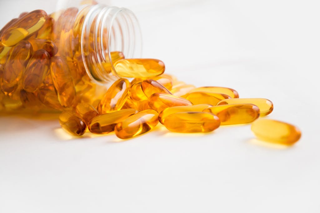 Close-up of fish oil omega-3 capsules spilling from a bottle on white background.