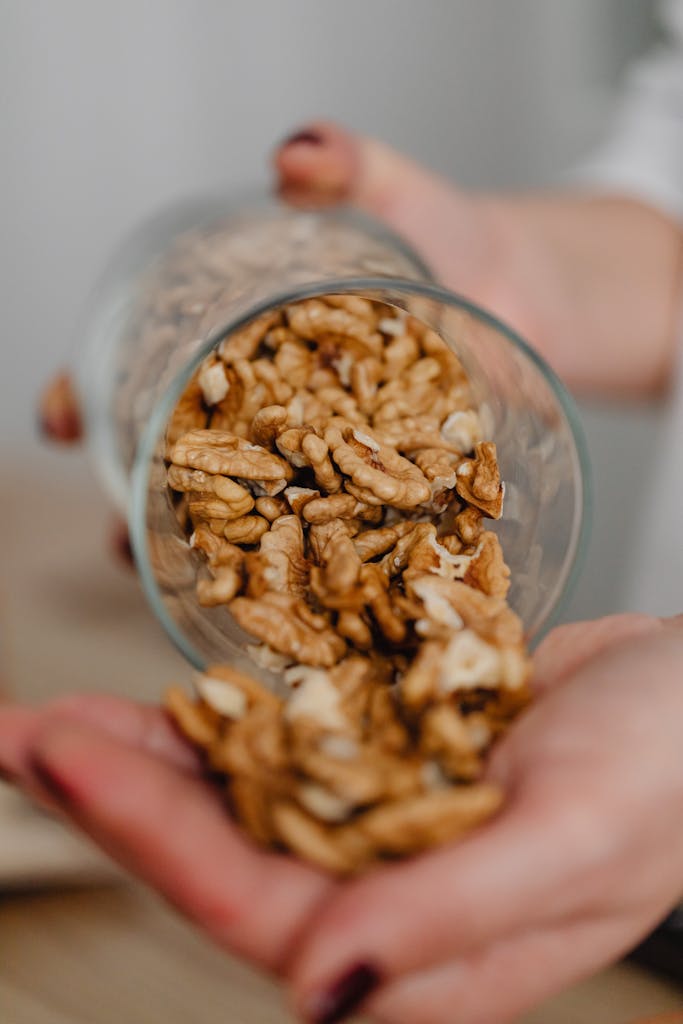 Close-up of walnuts being poured from a glass onto hands, showcasing healthy snacks.