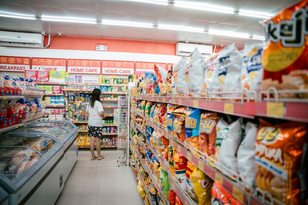 A woman browsing snack shelves at a supermarket, surrounded by various chips packages, hidden gluten explained.