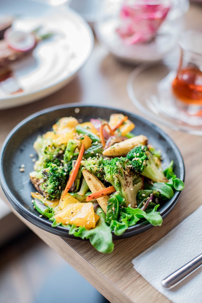 Close-up of a fresh vegetable salad with broccoli, carrots, and bell peppers on a black plate.