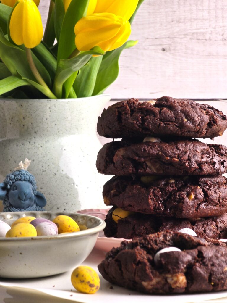 gluten-free chocolate mini egg cookies stacked with flowers and eggs.