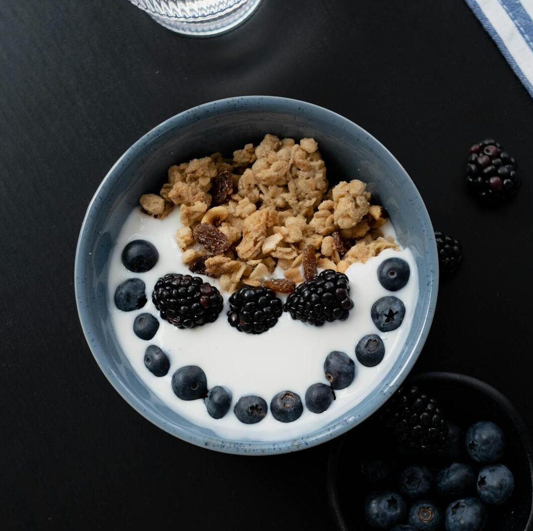 A healthy breakfast bowl with yogurt, granola, blackberries, and blueberries on a dark surface.